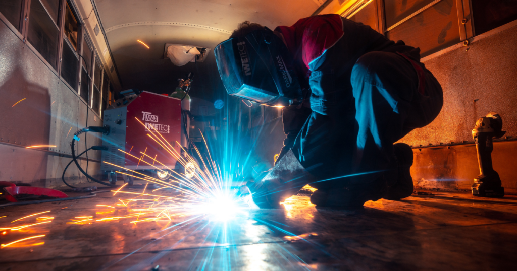 Stock photo of a person in protective clothing welding something on a metal floor.