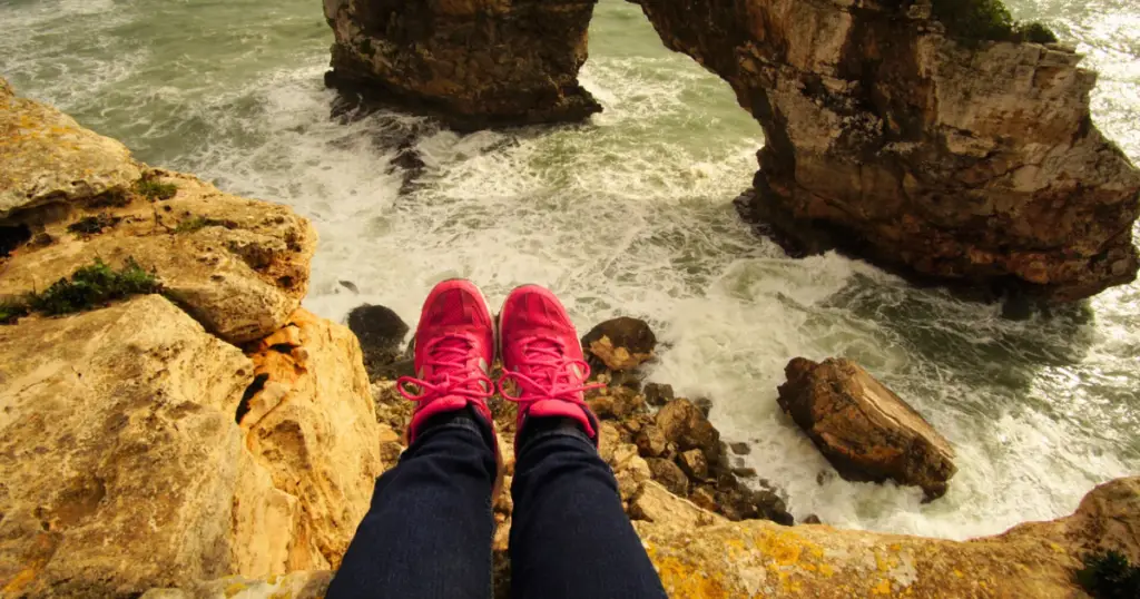 Stock photo of a person sitting with their legs over the edge of a rocky ledge over the ocean.