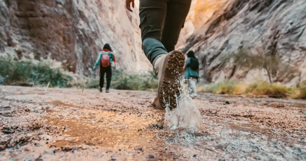 Stock image of people walking outside on a trail, with a foot walking through water in the foreground.