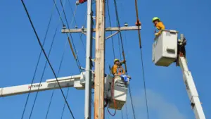 Two people in booths on cranes working on a powerline in daytime.