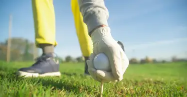 Stock photo, closeup of someone wearing golf gloves picking up a golf ball outside.