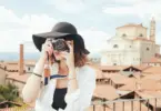 Stock photo of a woman taking a picture with a camera in front of a European city by the sea.