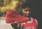 Man in a basketball jersey holding up a red basketball shoe.
