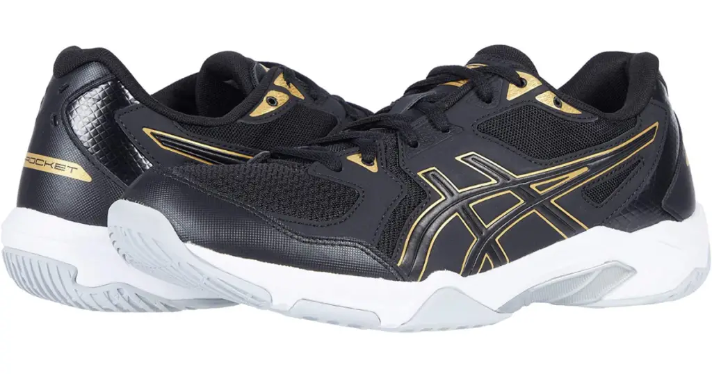 Closeup of Asics Gel Rocket 10. They are two black shoes with gold detailing on the Asics symbol on the sides and white soles.