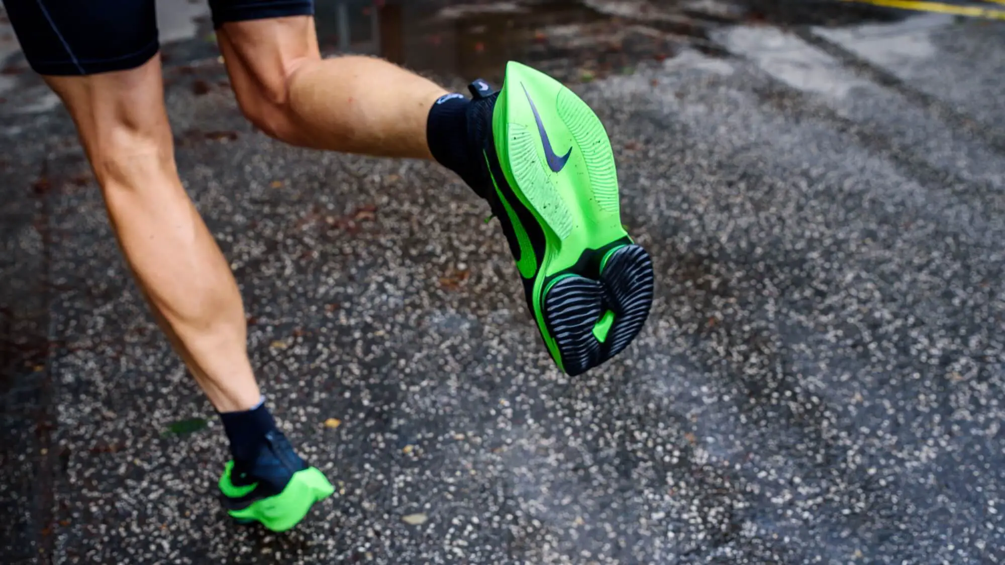 Man running on wet road with green and black nike running shoes.
