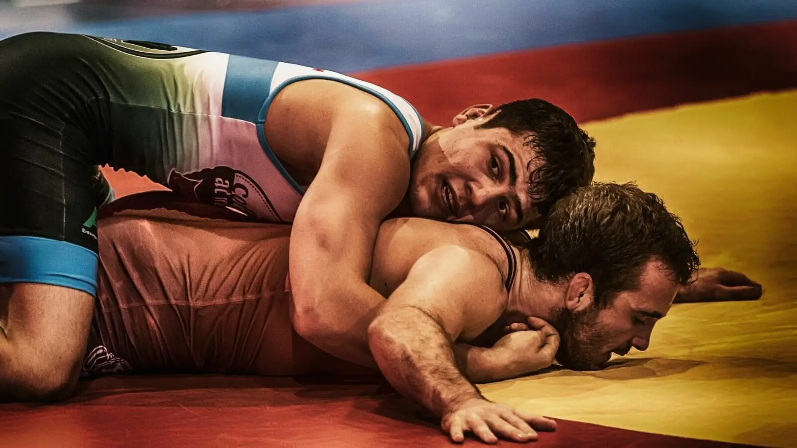 Wrestling being pinned during training on red and yellow mat.