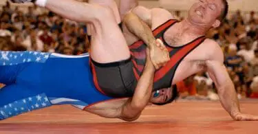 Two wrestlers hitting the mat with wrestling shoes visible in the air