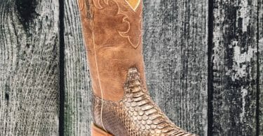Snakeskin cowboy boot on weathered wood background.