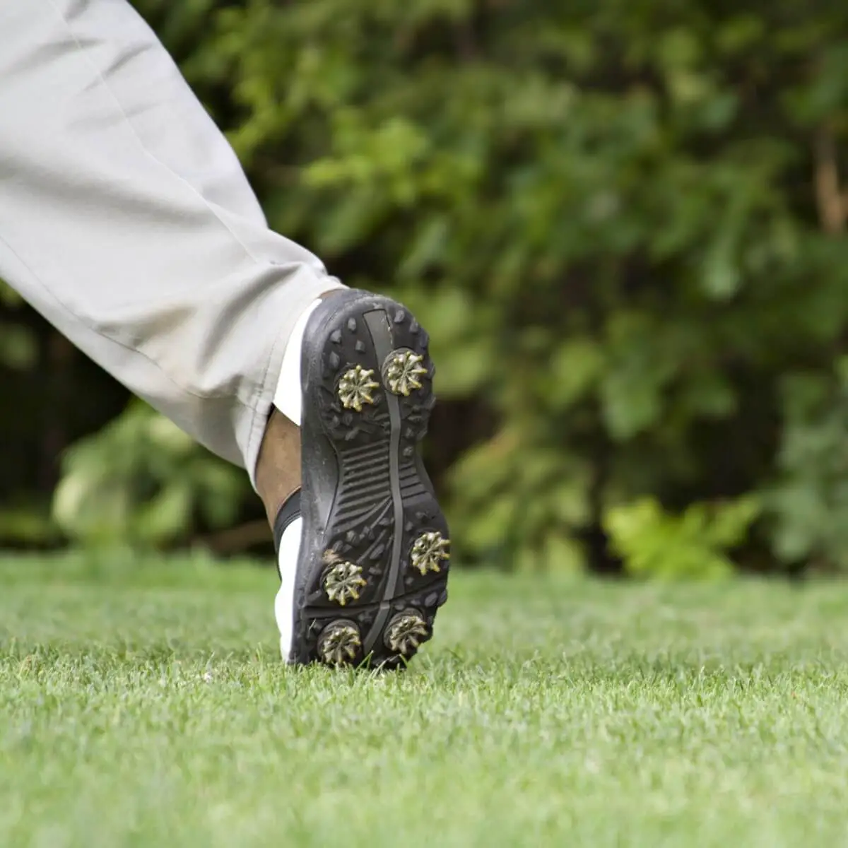 Man in golf spikes walking of the 18th green.