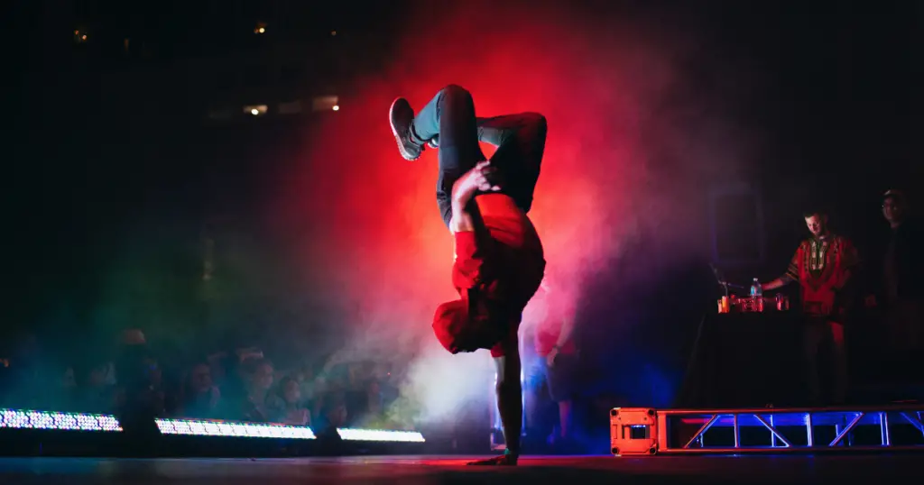 Stock photo of a person doing a one-arm handstand on a stage, dancing hip-hop.