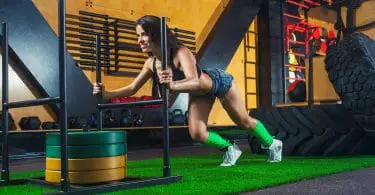 Woman pushing sled with 100kg weights using some of the best CrossFit shoes for traction.