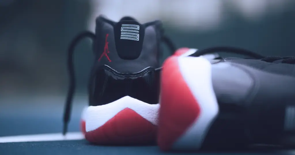 Two Air Jordan basketball shoes (black, with white and red soles) from the back, one shoe (right) on its side.