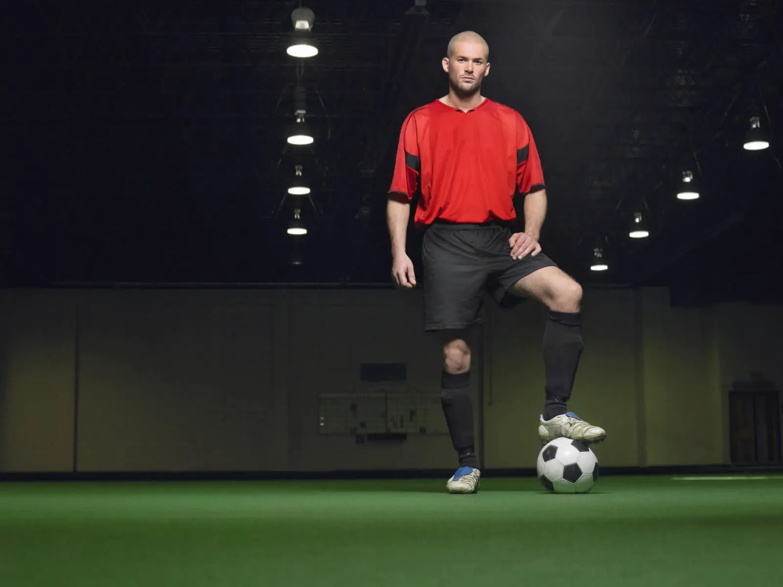 Man standing in indoor soccer arena with ball.